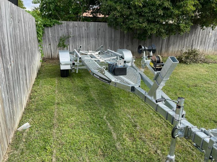 Boat Trailer Parked On Green Grass Next To A Wooden Fence — In Tune Marine in Mackay, QLD