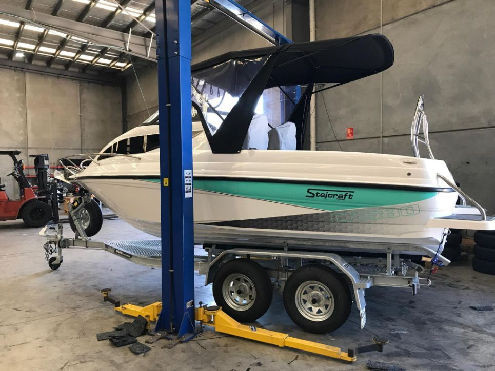 White Boat On A Trailer In A Garage, Lifted By A Blue Car Lift. Teal And Black Accents — In Tune Marine in Mackay, QLD