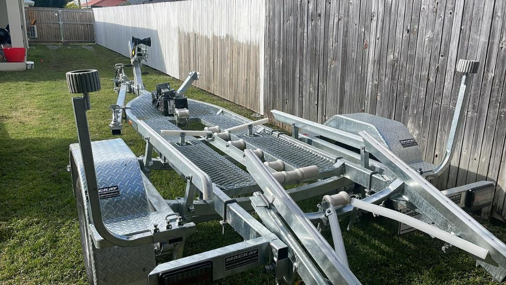 A Boat Trailer Sits On Green Grass Next To A Wooden Fence; Bright Sunny Day — In Tune Marine in Mackay, QLD