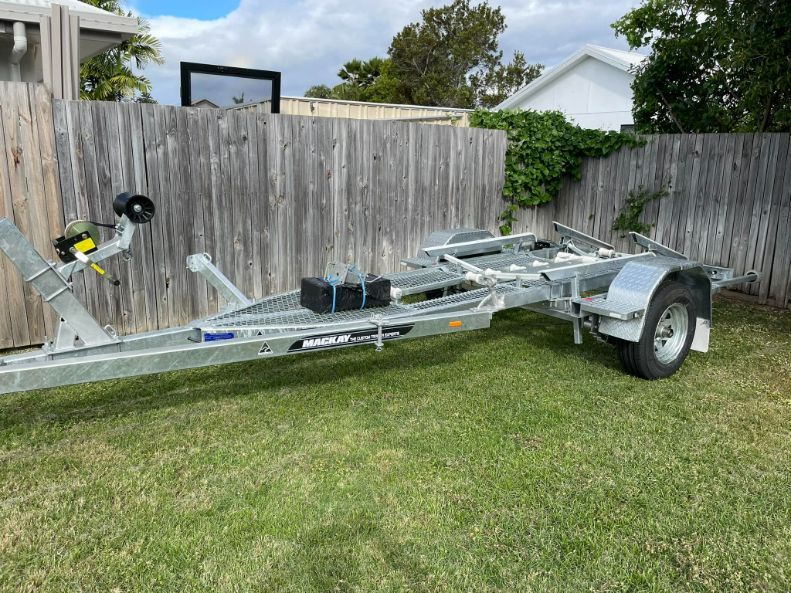 Boat Trailer Parked On Grass Next To A Wooden Fence On A Sunny Day — In Tune Marine in Mackay, QLD