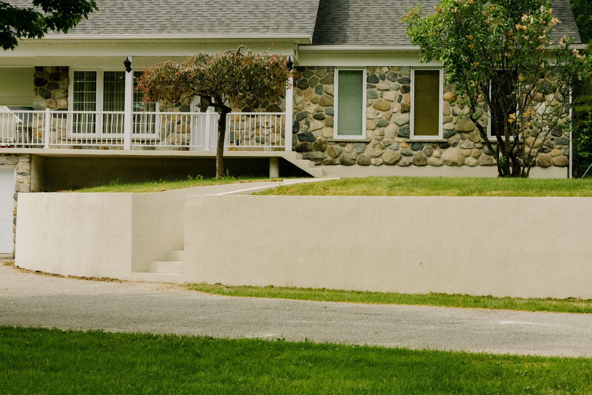 Mur de soutènement beige devant une maison en pierre et stuc avec un porche et une allée.