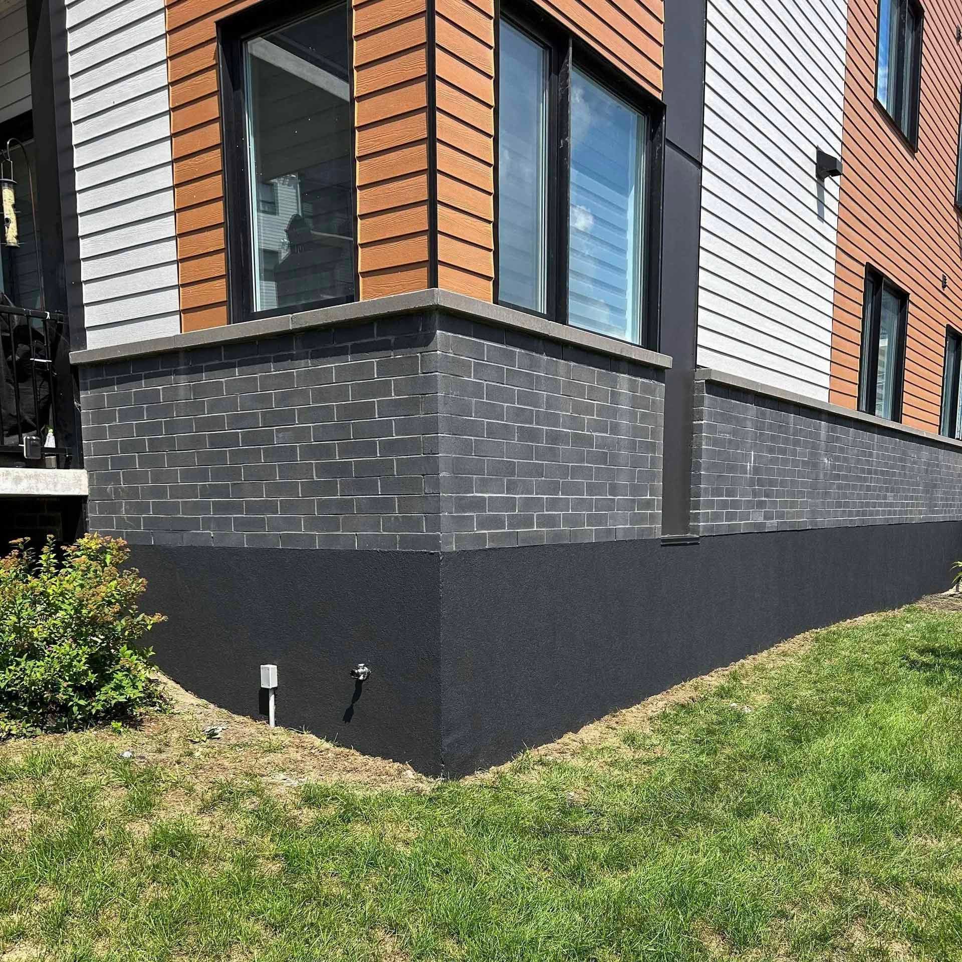 Extérieur d'un bâtiment moderne avec briques noires et revêtement, pelouse herbeuse.