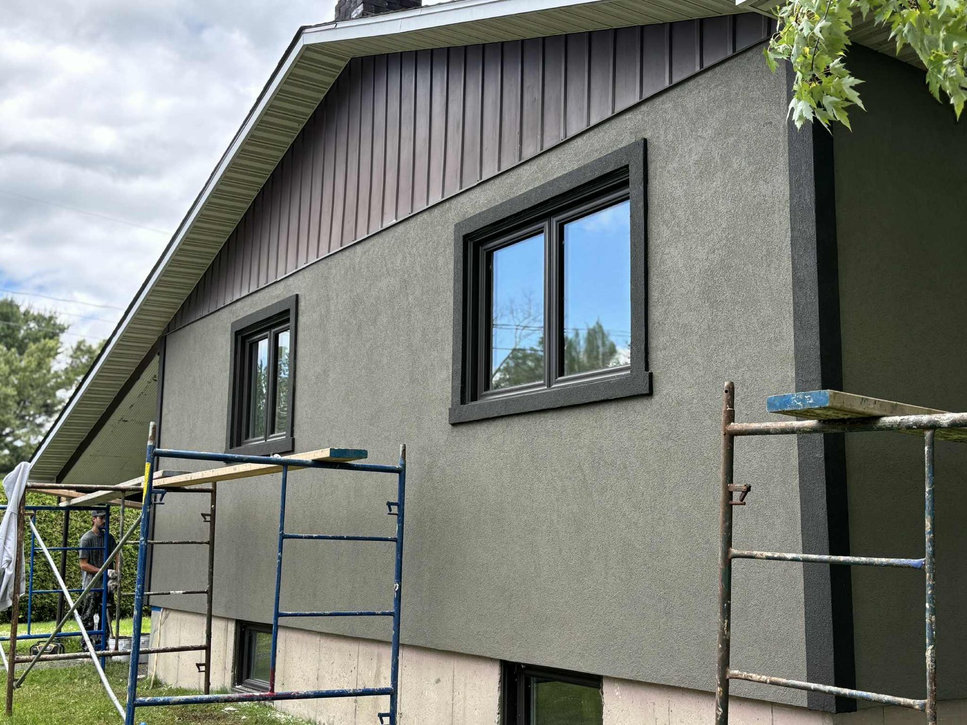 Extérieur de la maison avec revêtement en stuc, garniture brun foncé autour des fenêtres, échafaudage.