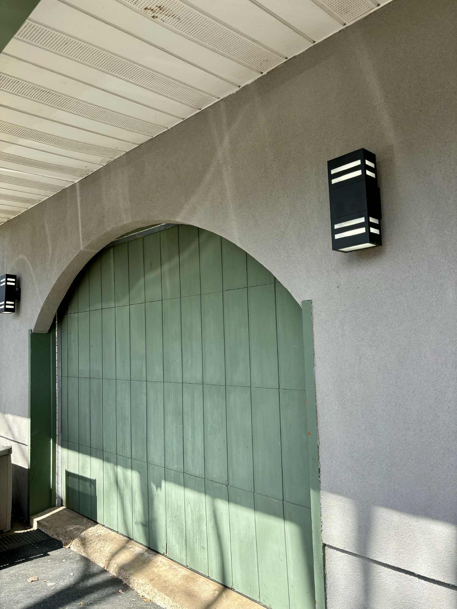 Porte arquée verte avec deux appliques murales noires sur un extérieur en stuc gris.