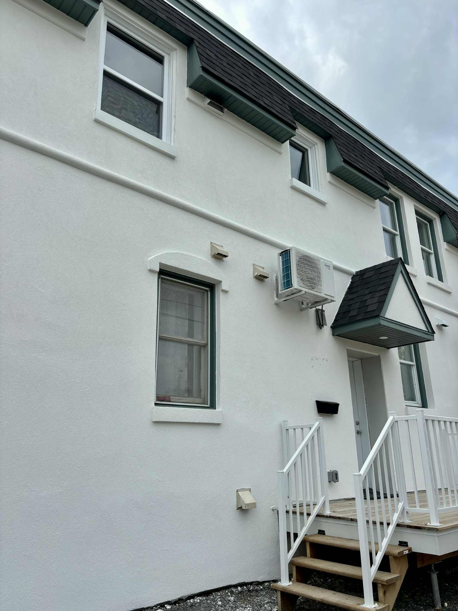 Bâtiment en stuc blanc avec plusieurs fenêtres, un petit porche et une unité de climatisation.