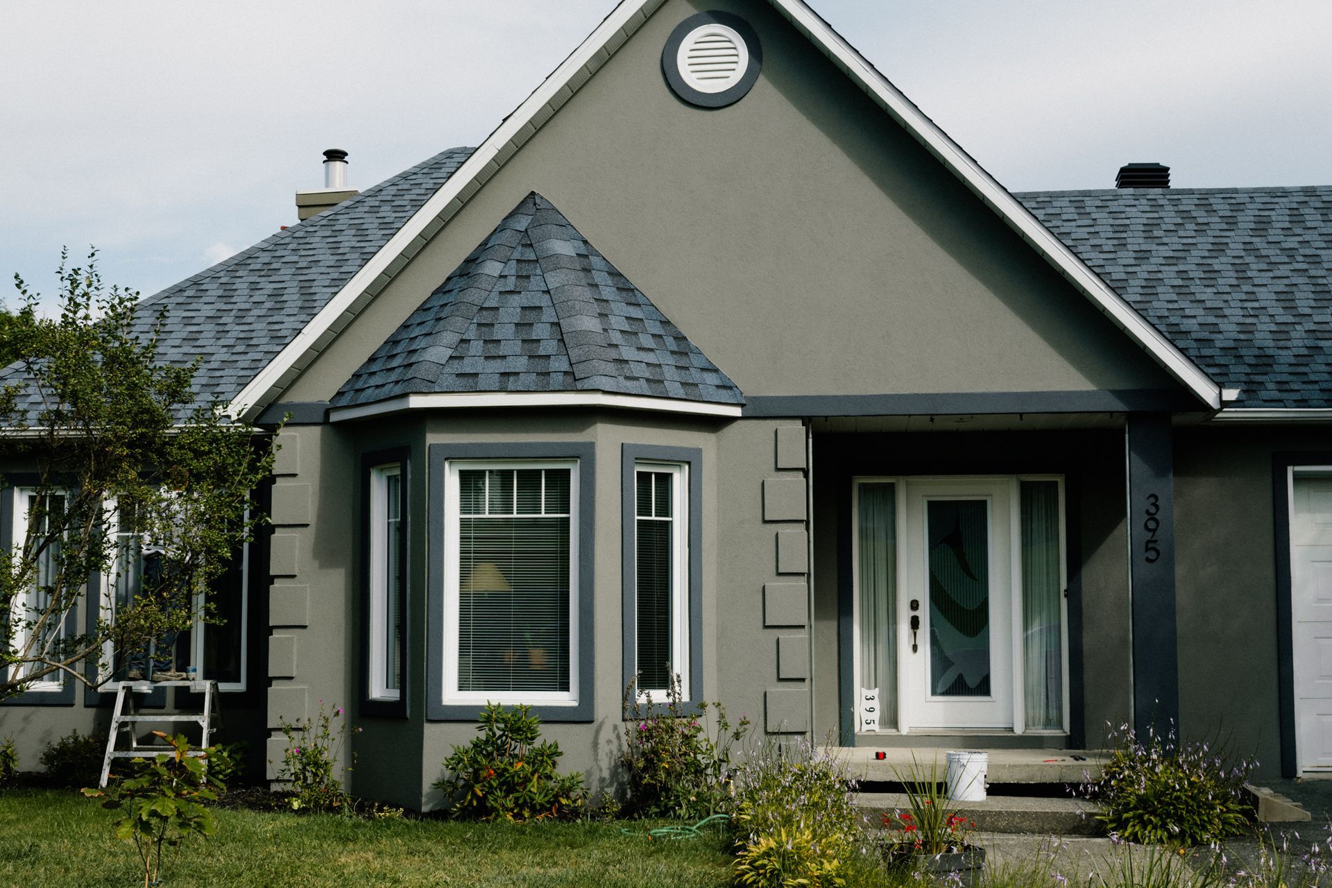 Maison en stuc gris avec garnitures foncées, fenêtres et porte blanches, petite cour avant.