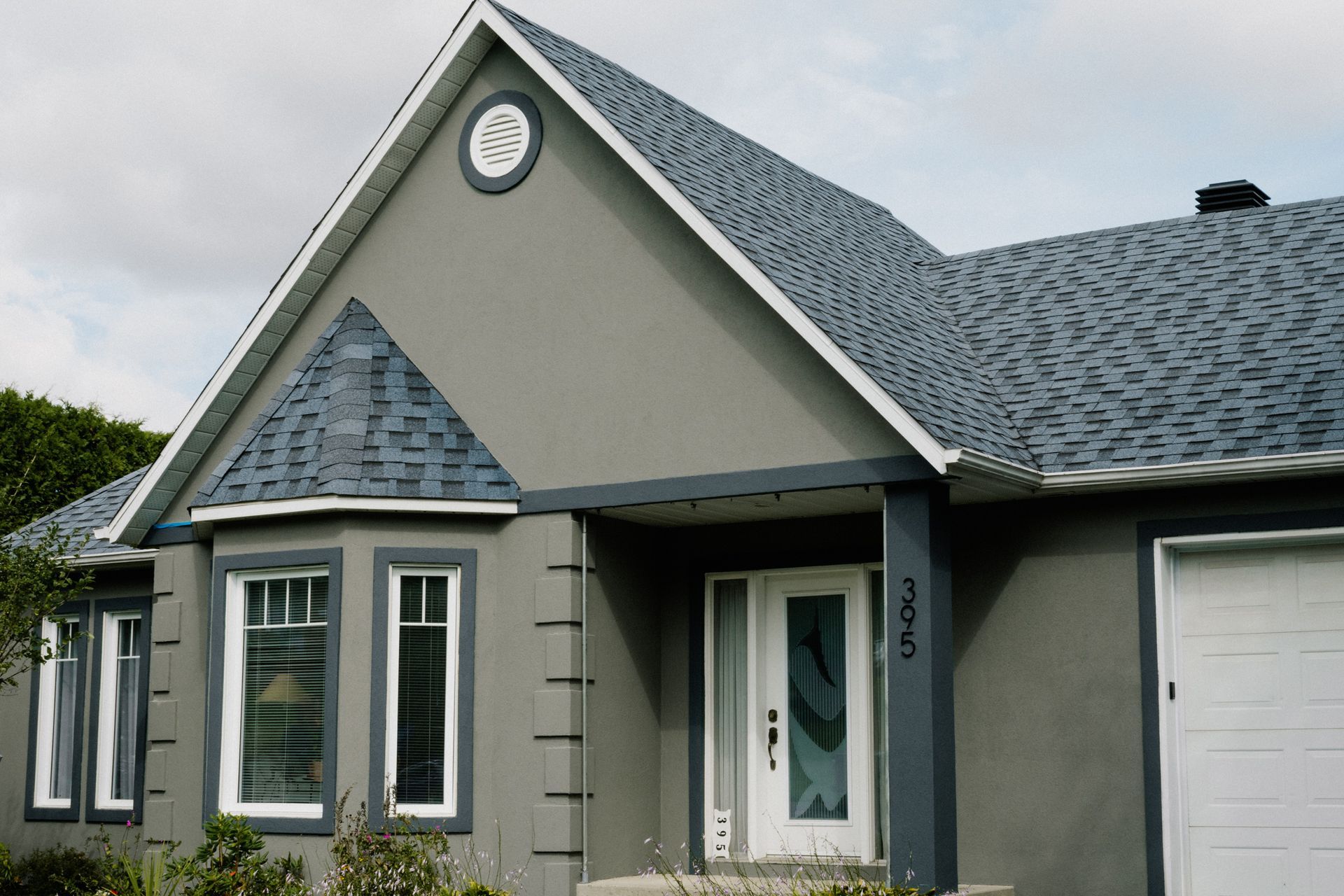 Maison grise avec des garnitures blanches, un toit bleu et une porte d'entrée blanche.