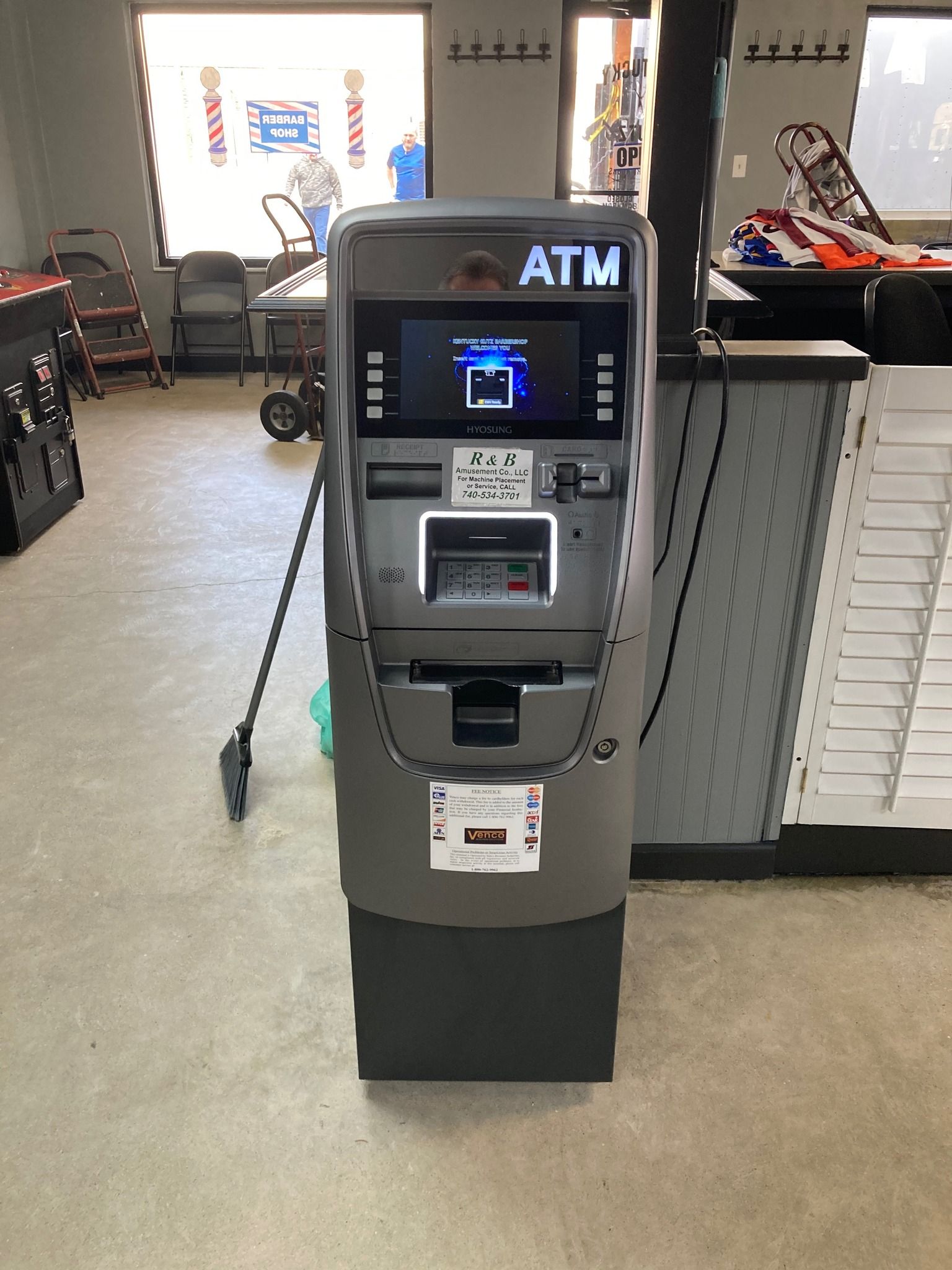 Man at ATM inserting card, smiling. He wears a tie, carrying a bag and phone. Indoor setting.