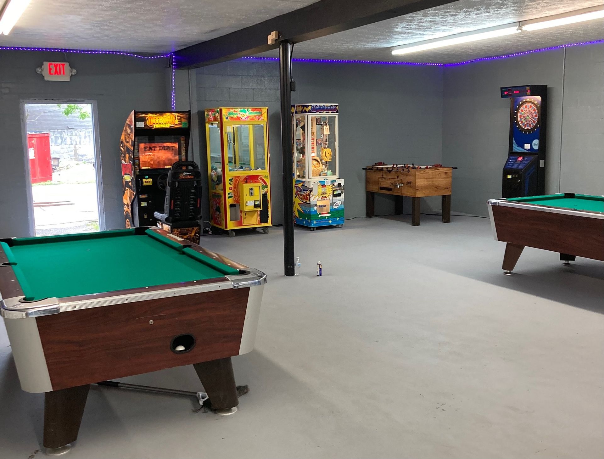 Game room with pool table, arcade games, foosball, and a dart board. Gray walls, open doorway.