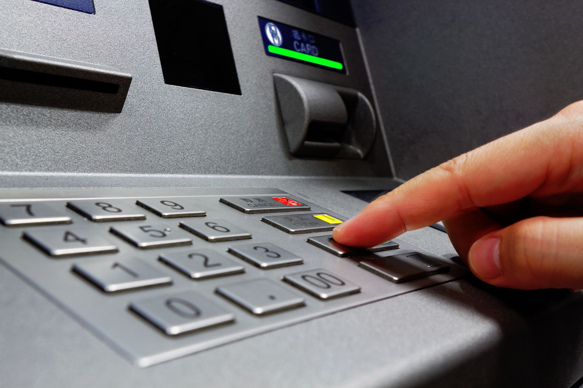 A close-up view of a hand pressing a button on a gray ATM numeric keypad.