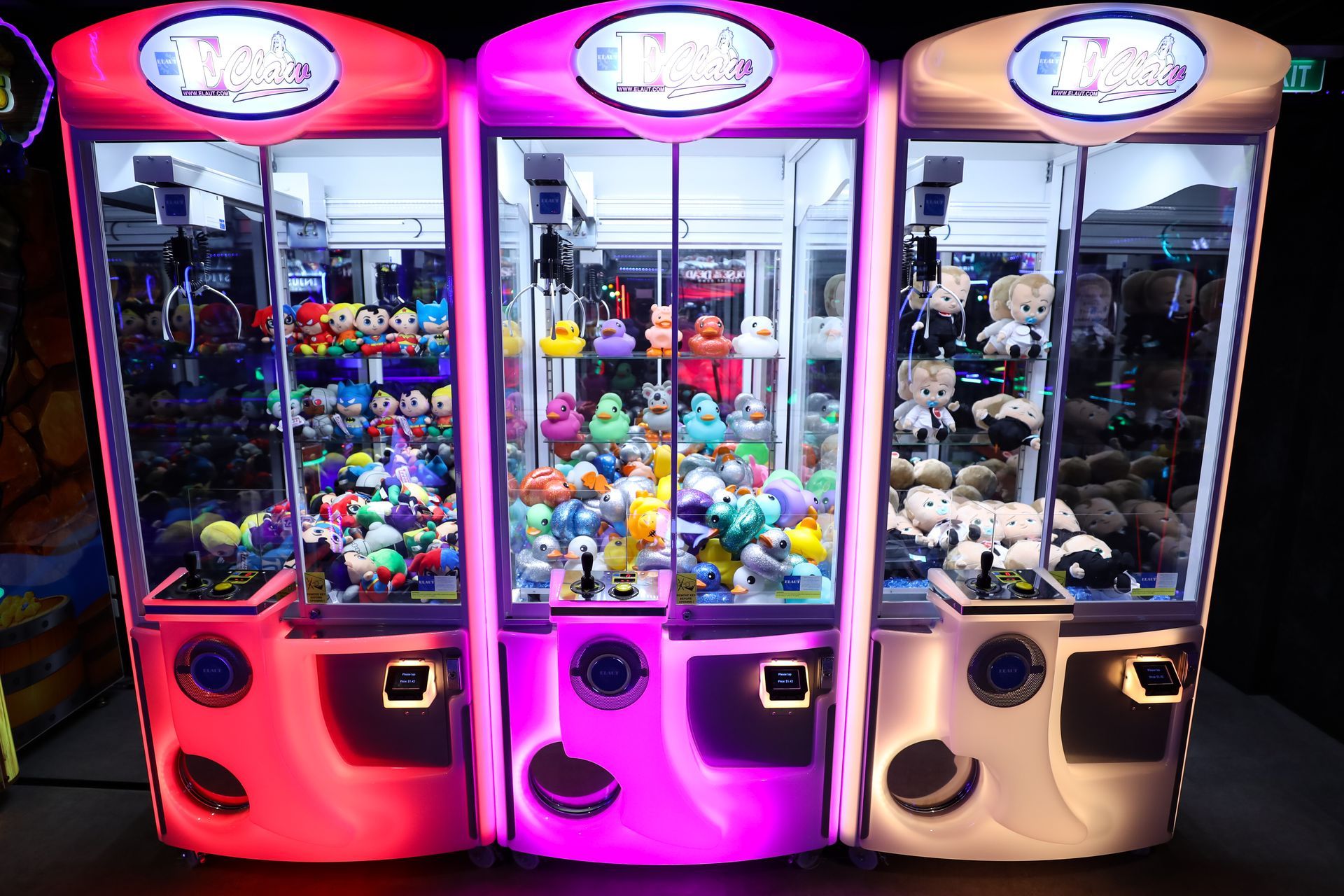 Three brightly lit claw machine arcade games with plush toys inside.