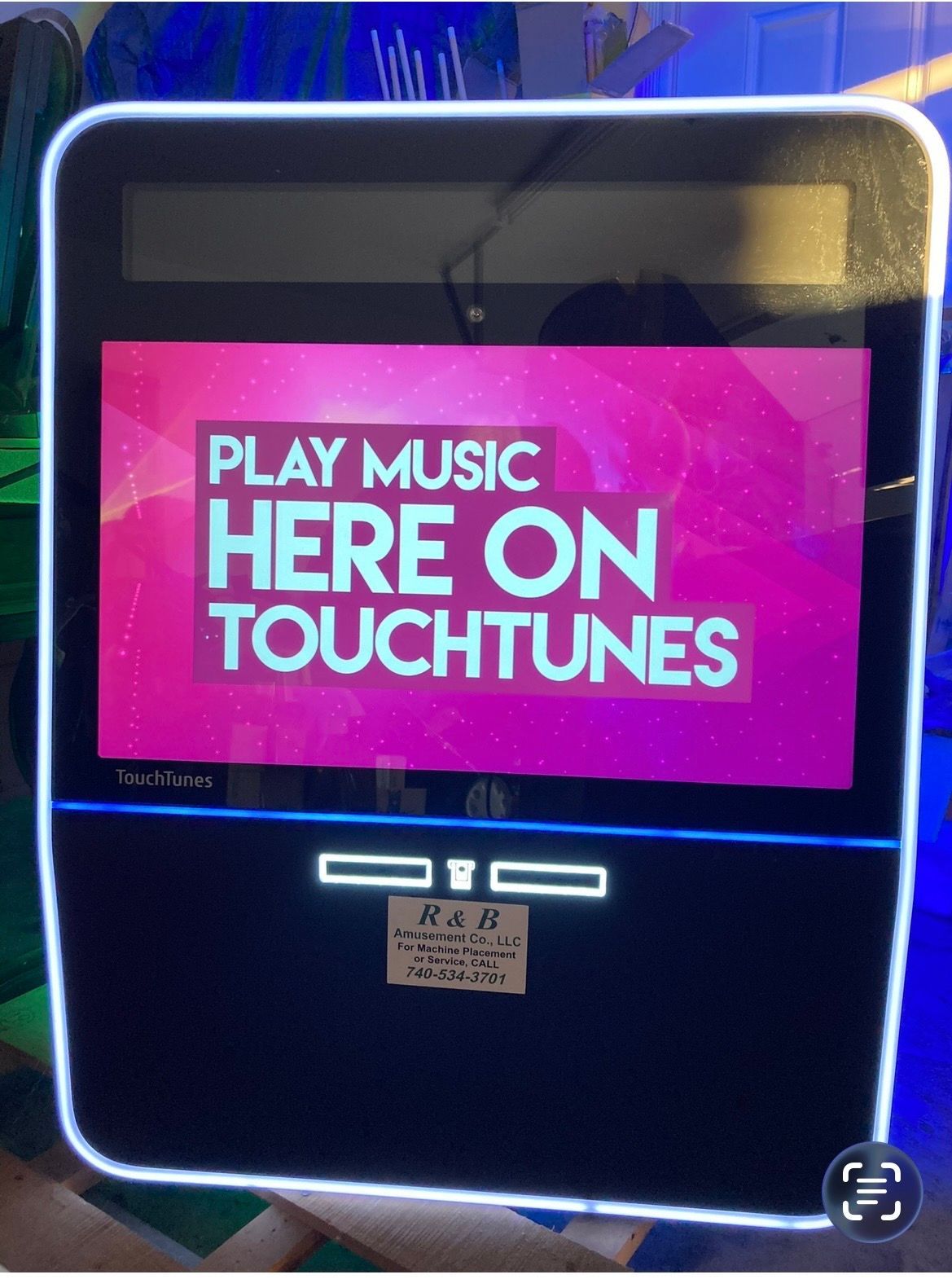 A TouchTunes digital jukebox with a neon-lit frame displaying 