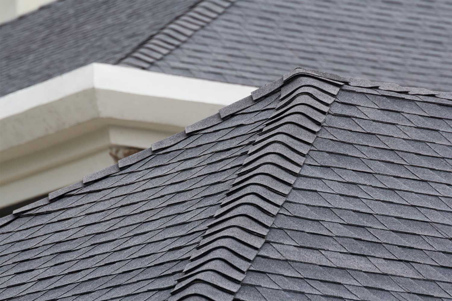 Close-up of gray asphalt shingle roof with ridge cap on residential home.
