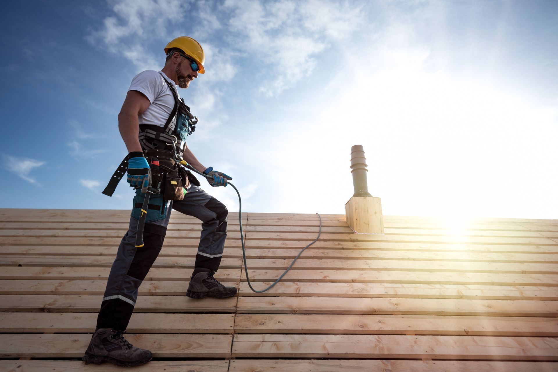 A roofer with a safety harness and tool belt standing on a roof.