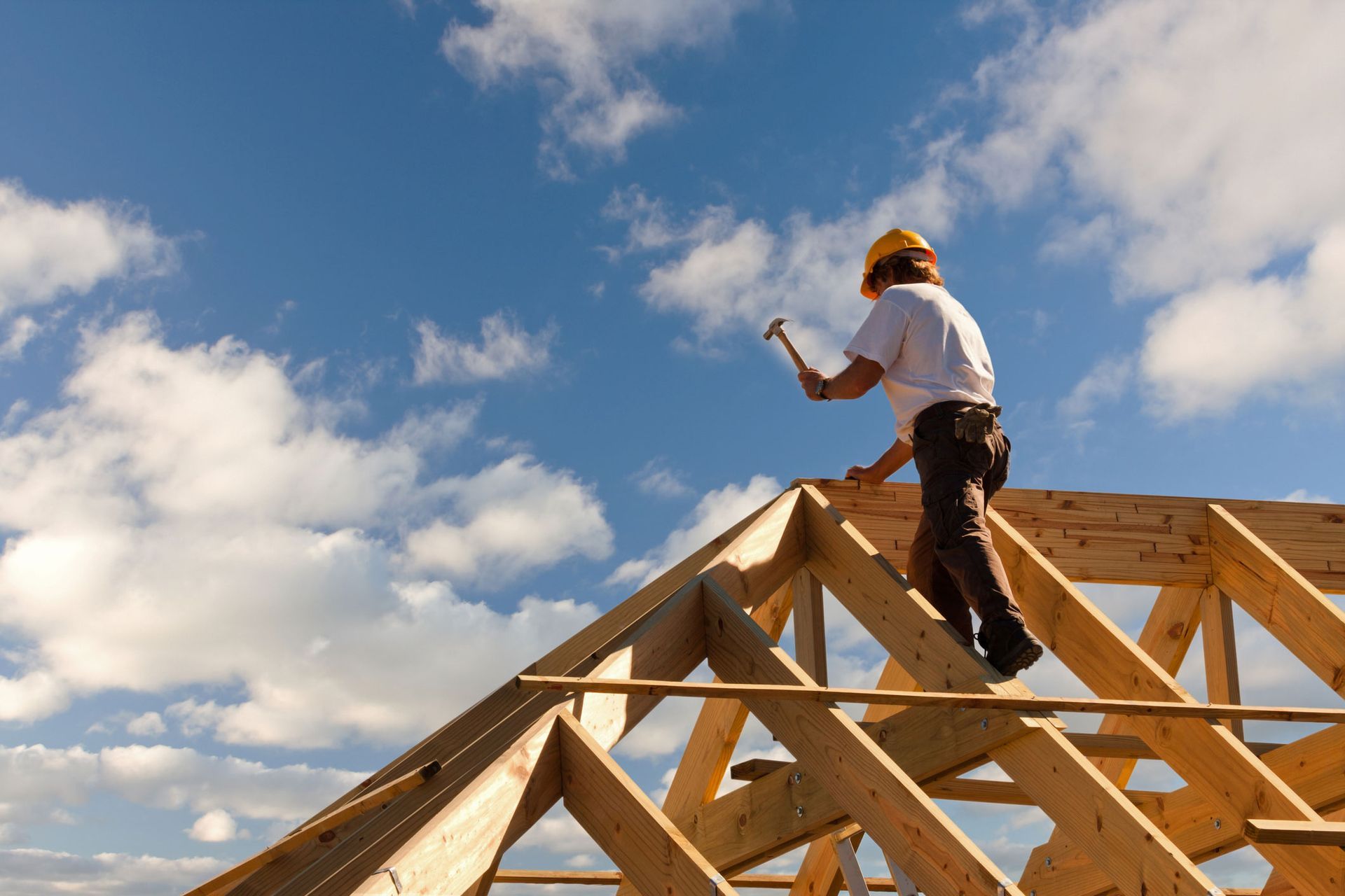 Construction worker building wooden roof frame on house under blue sky with scattered clouds. Construction worker building wooden roof frame on house under blue sky with scattered clouds.