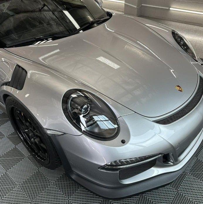 A silver Porsche 911 GT3 RS parked in a garage with grey interlocking floor tiles.