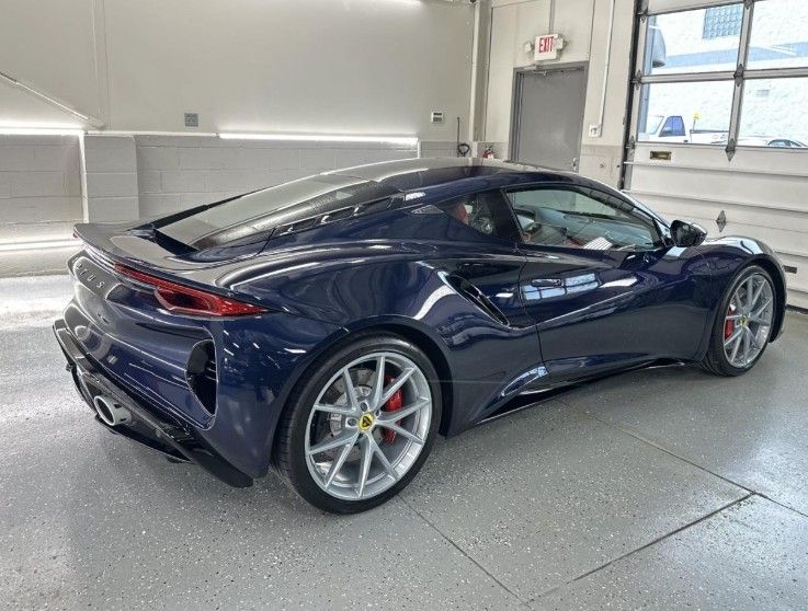 A dark blue Ferrari sports car parked at an angle inside a bright, clean garage with white walls and grey floors.