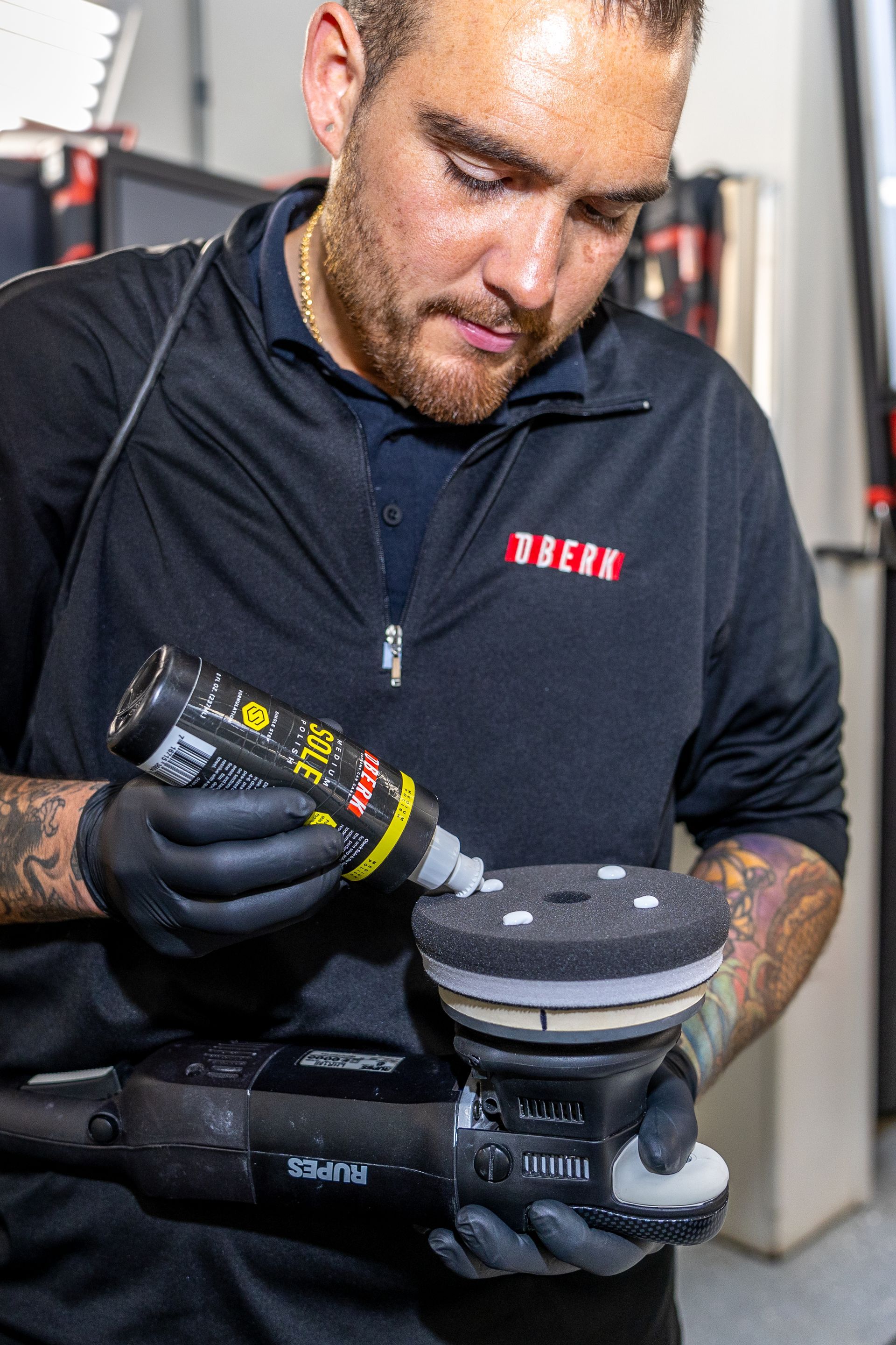 A man is polishing a red sports car in a garage.