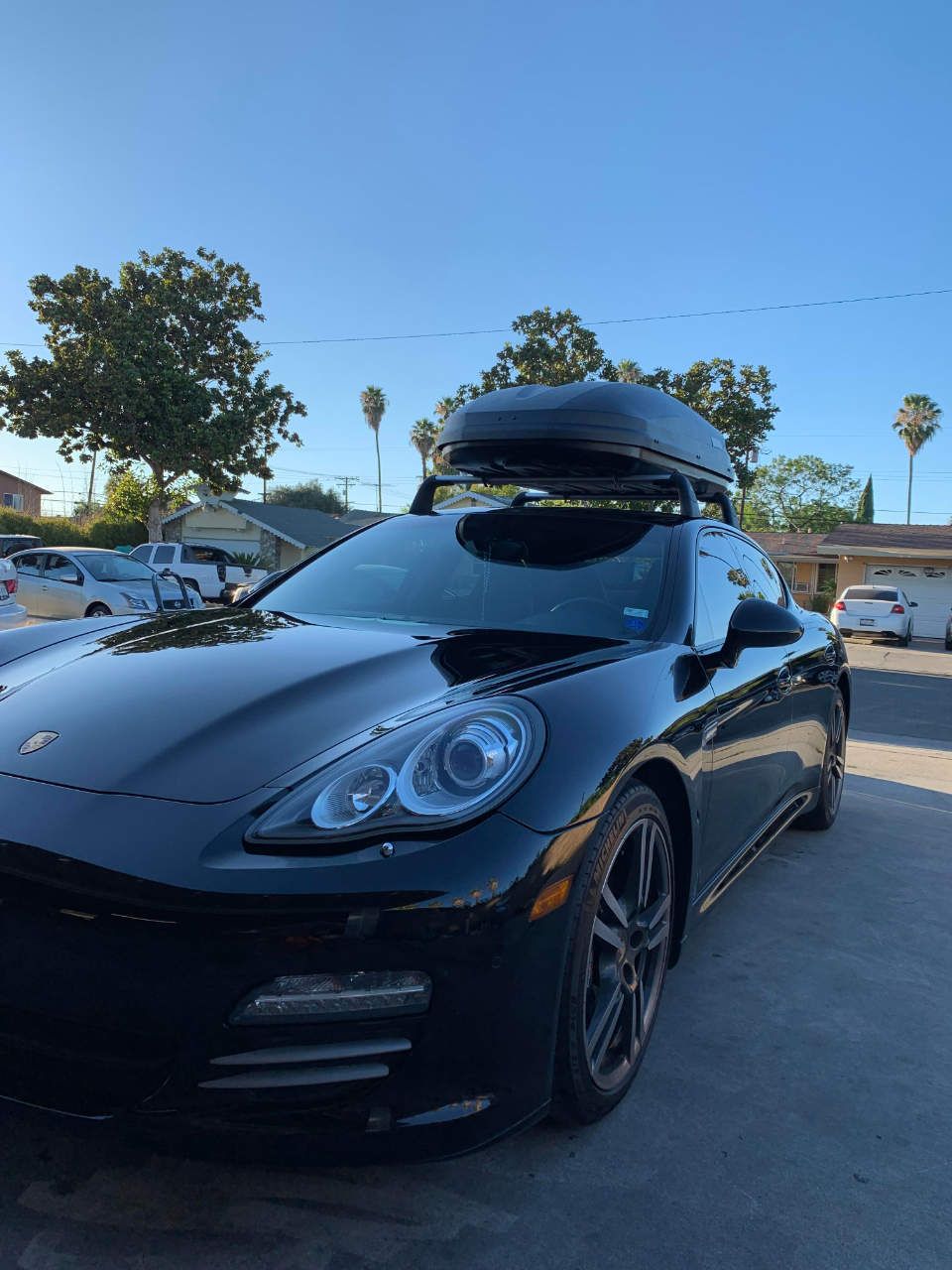 Black Porsche sports car parked outdoors with rooftop cargo box under a clear blue sky