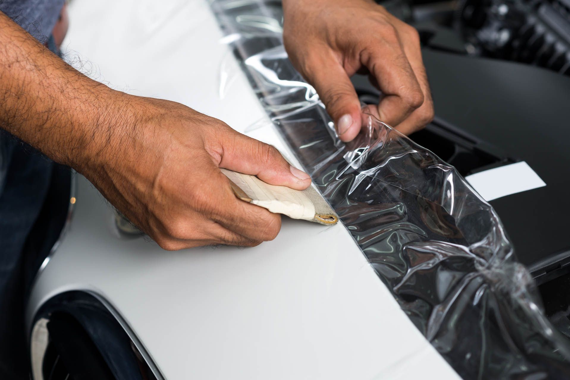 Hands installing clear protective film on a white car.