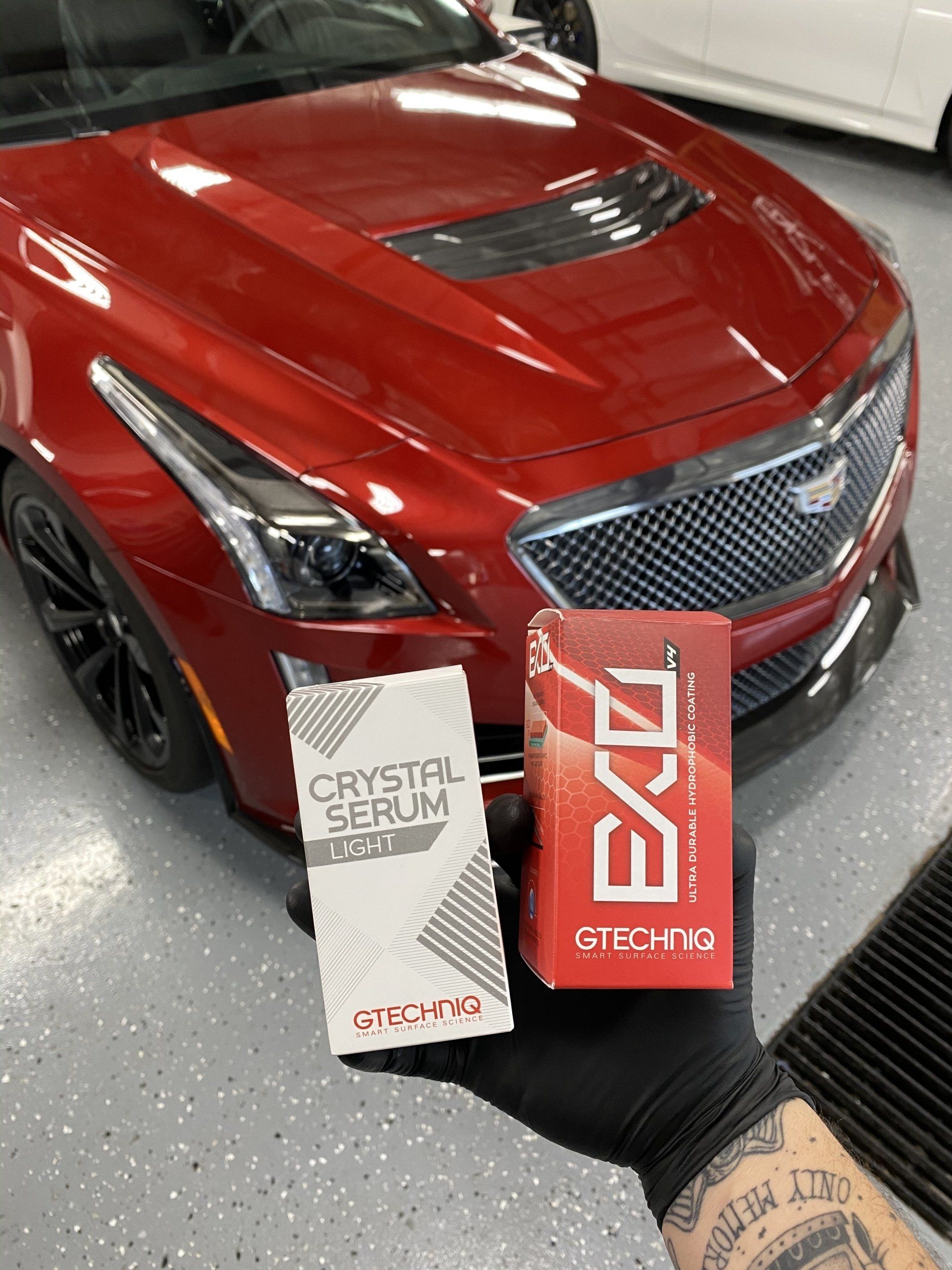 A person is holding a box of crystal serum in front of a red car.