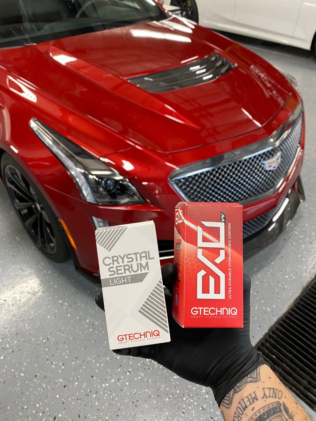 A person is holding a box of excel crystal serum in front of a red car.