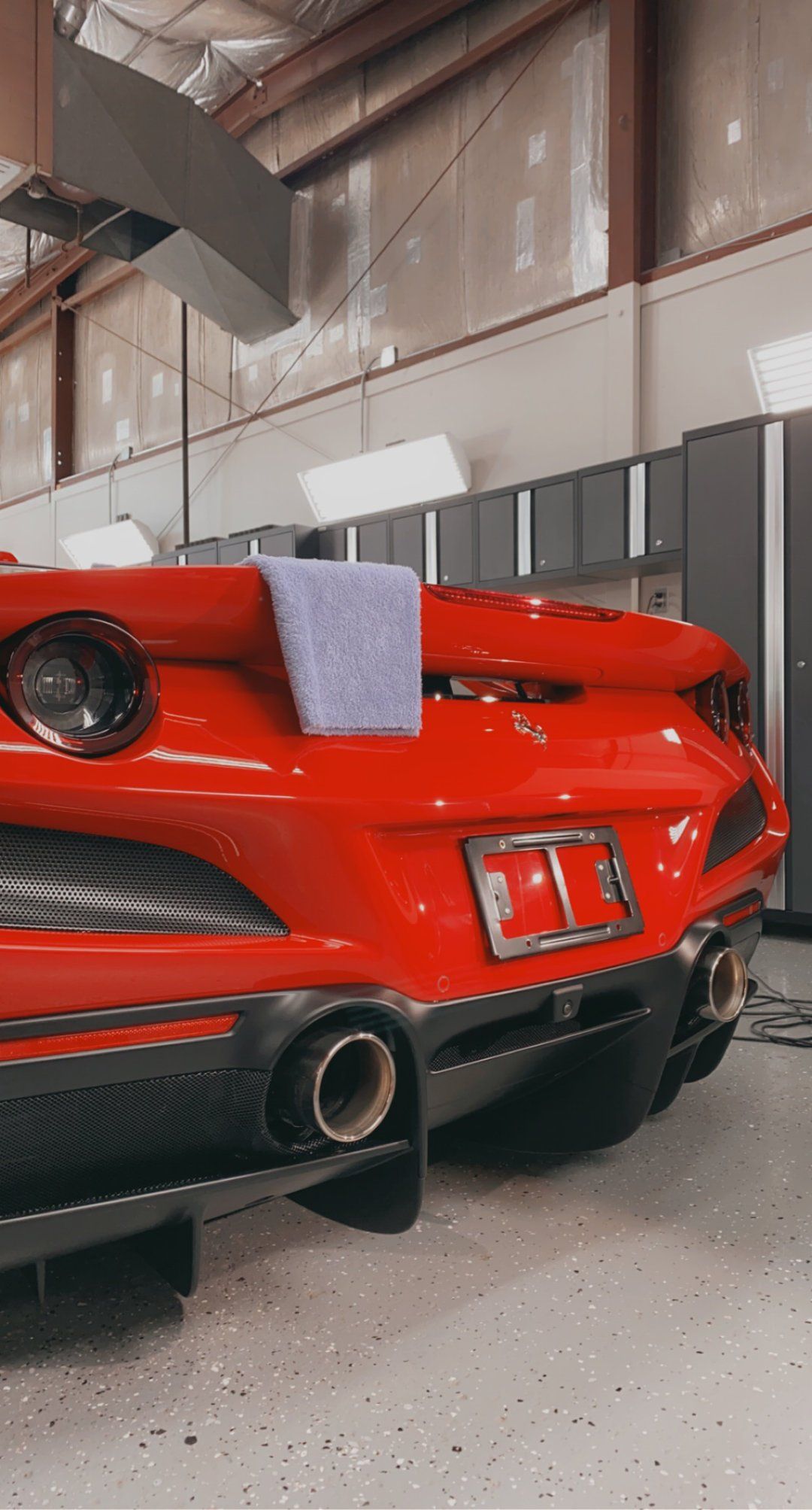A red sports car is parked in a garage with a towel on the hood.