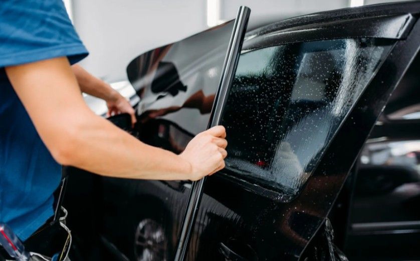Person applying tint film to a car window. Black car in a workshop setting.
