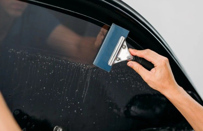 Person applying window tint to a car window with a squeegee.