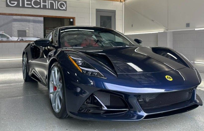 Dark blue Lotus Emira sports car in a garage with red interior, Gtechniq sign.