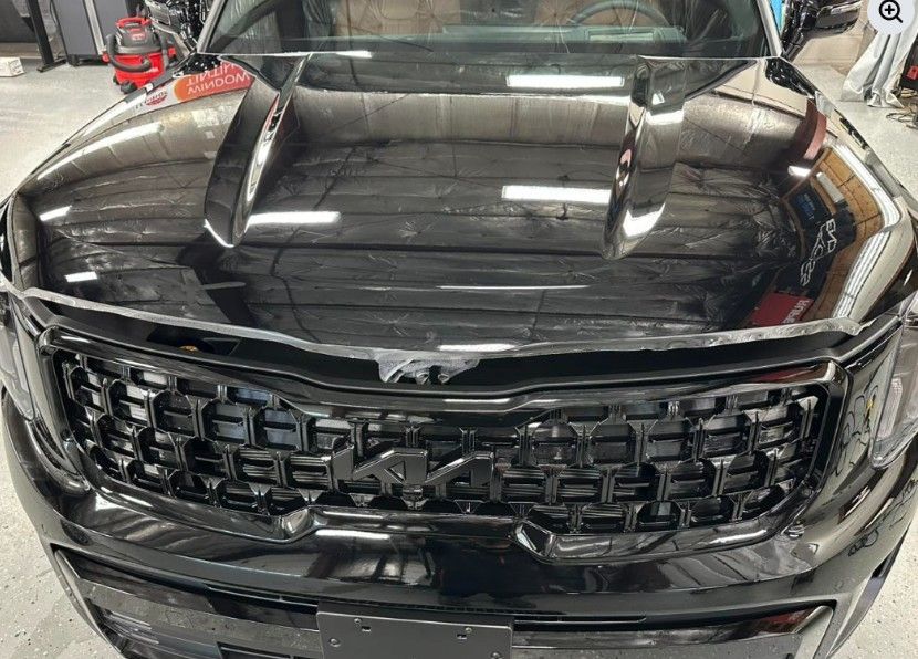 Black Kia Telluride front with grill and hood, likely being worked on in a shop.