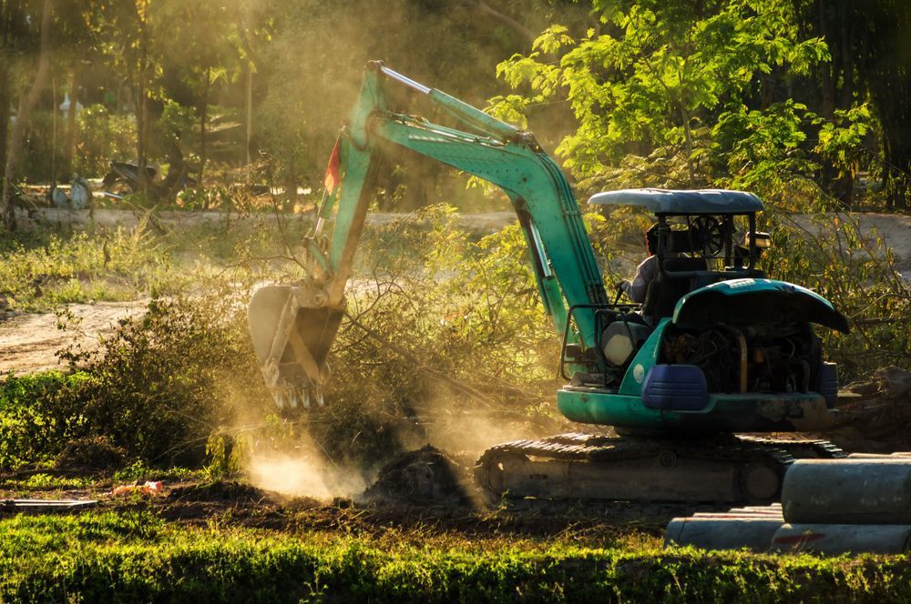A Man Is Driving An Excavator In A Field — JC Hire In Bli Bli, QLD