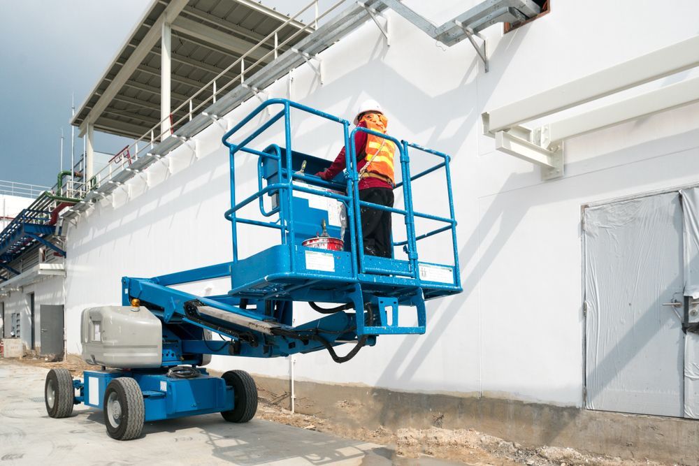 A Man Is Sitting On A Blue Aerial Lift In Front Of A Building — JC Hire In Bli Bli, QLD