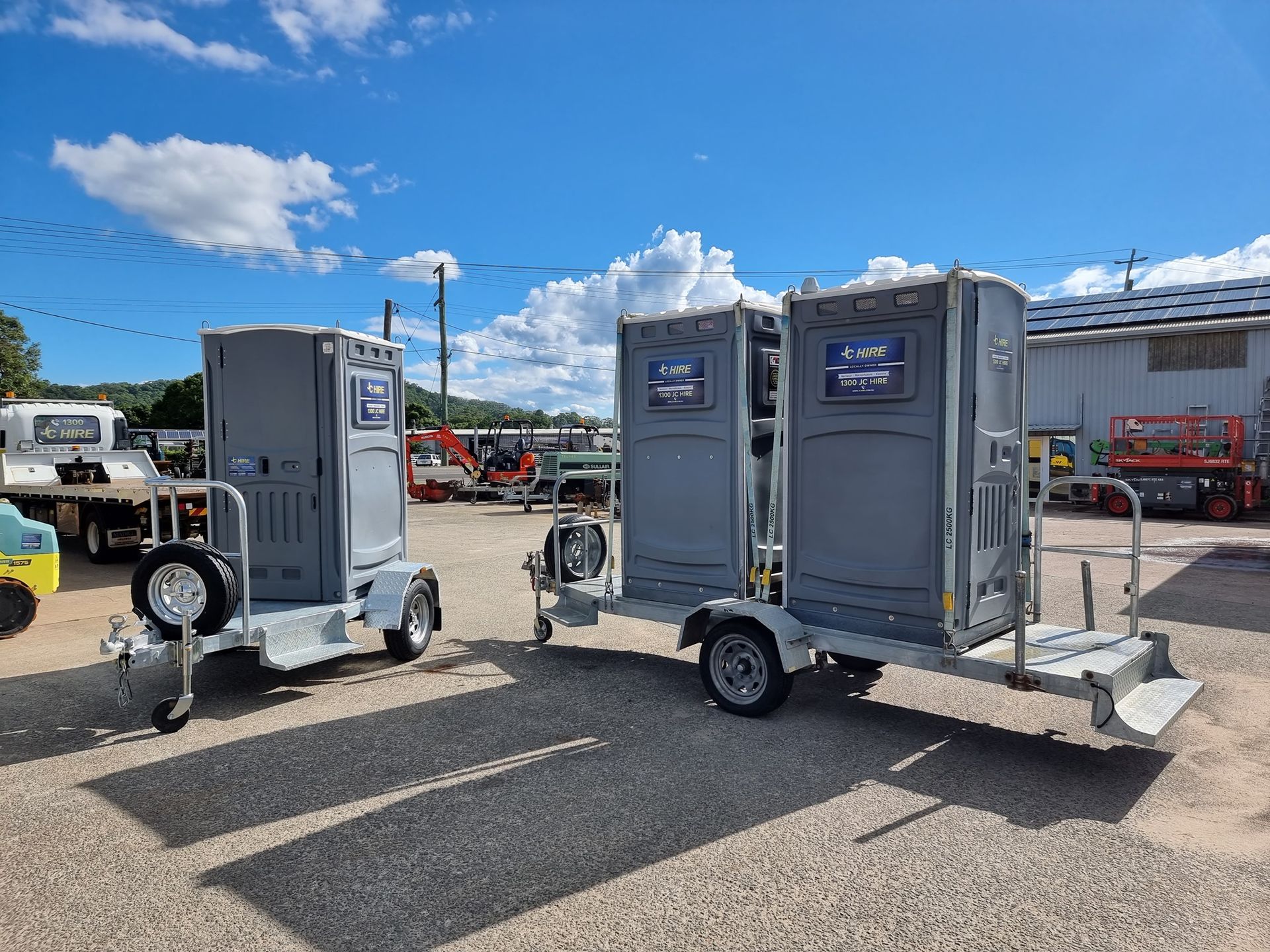 Two Grey Portable Toilets on Trailers in a Gravel Lot Under a Blue Sky — JC Hire In Bli Bli, QLD