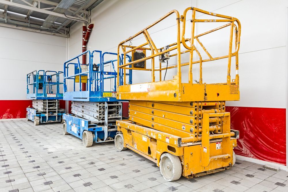 A Row Of Scissor Lifts Are Parked In A Warehouse — JC Hire In Nambour, QLD