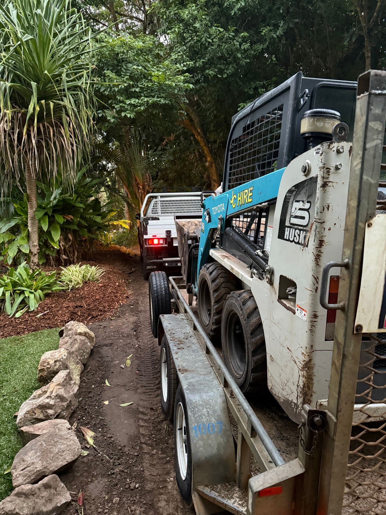 Blue Skid Steer Follows a White Truck Along a Muddy Forest Trail — JC Hire In Bli Bli, QLD
