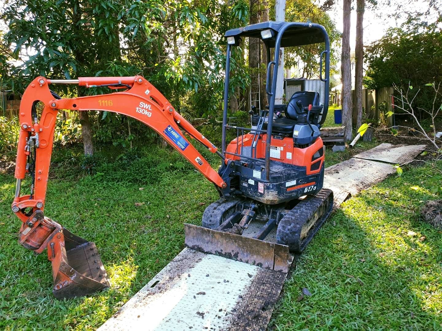 Orange Mini Excavator Digging Beside a Concrete Path in a Grassy Yard — JC Hire In Bli Bli, QLD