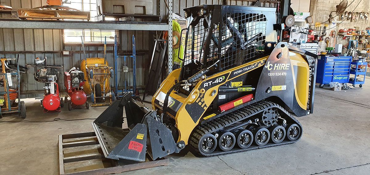 A Yellow And Black Tractor Is Parked In A Garage — JC Hire In Bli Bli, QLD