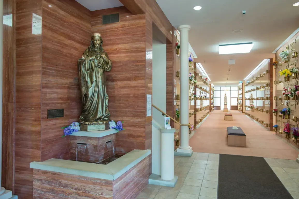 Hospital hallway with a statue in a wood-paneled alcove and shelves lining the corridor