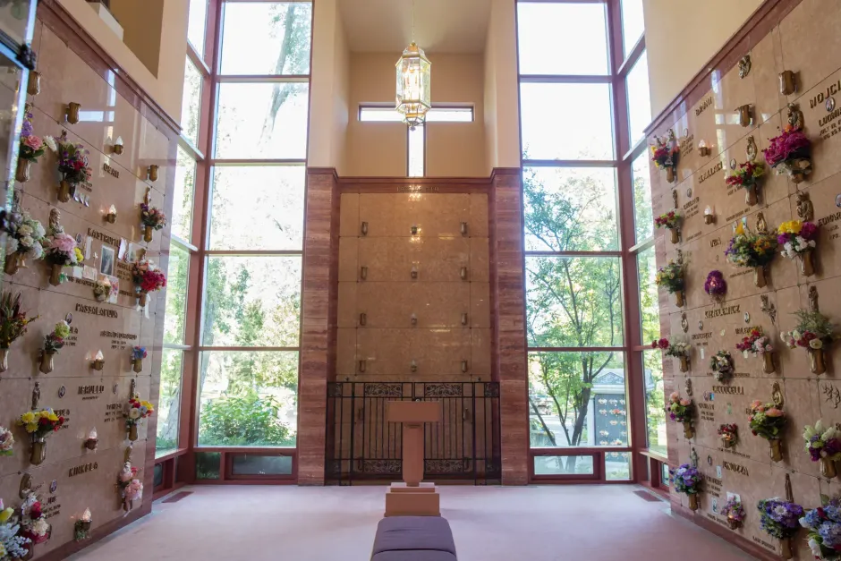 Memorial chapel interior with floral wall tributes, central altar, and tall windows