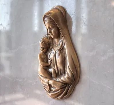 Relief sculpture of a veiled woman holding a child in soft bronze tones on a marble wall