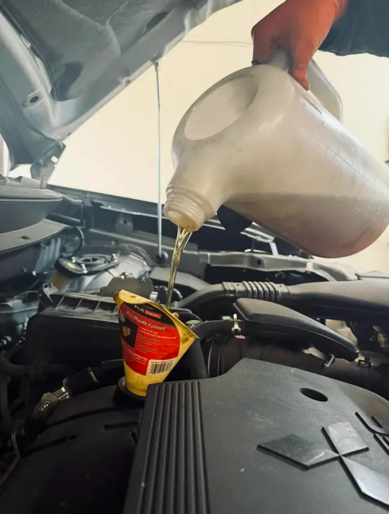 Person pouring oil into a car engine, using a funnel. | Supreme Auto Repair Shop