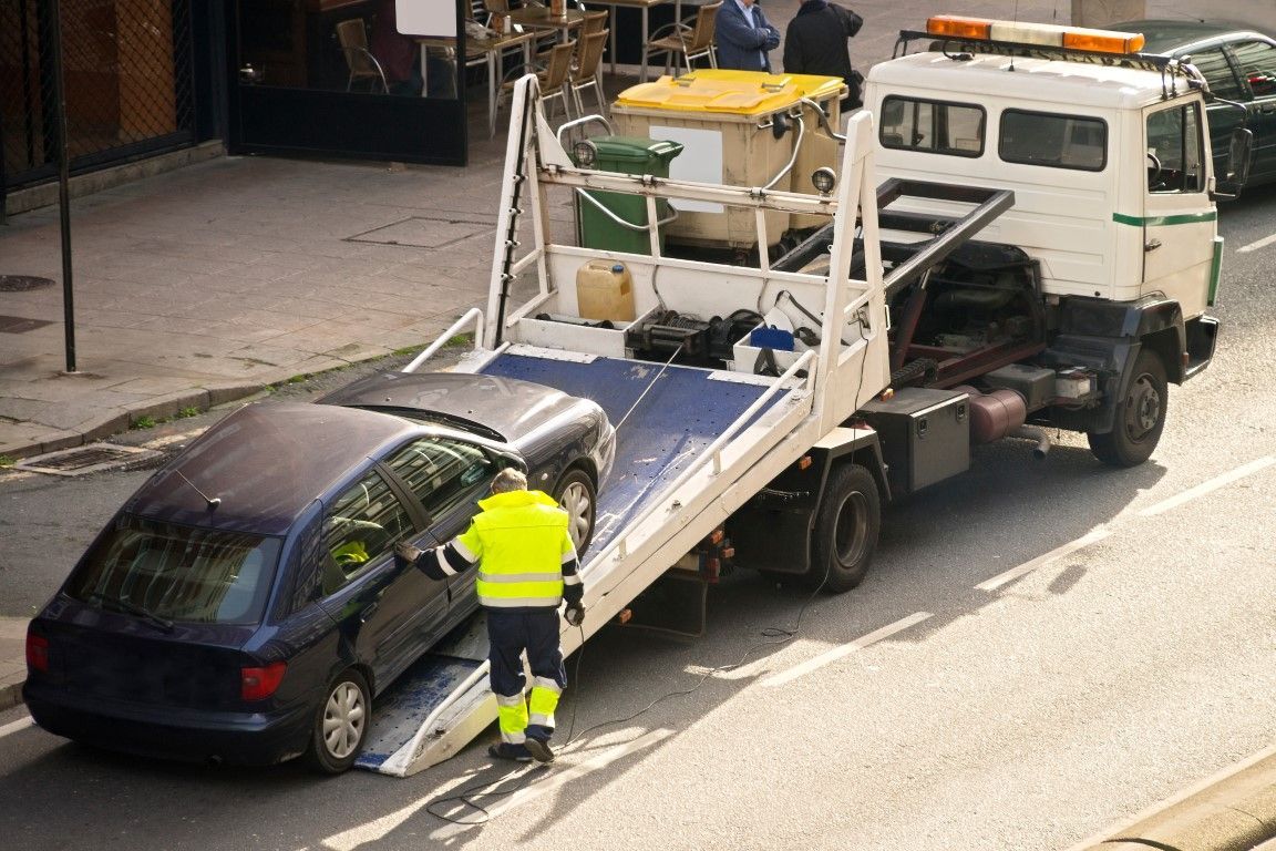 Illegally parked car being winched up on to flat deck tow truck 