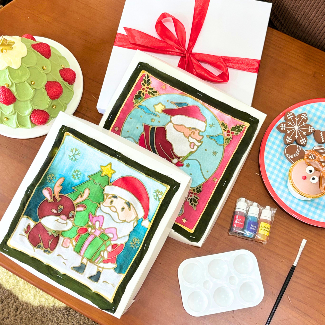 DIY batik Christmas artworks with festive designs, painting tools, and gift packaging arranged on a table at Jadi Batek