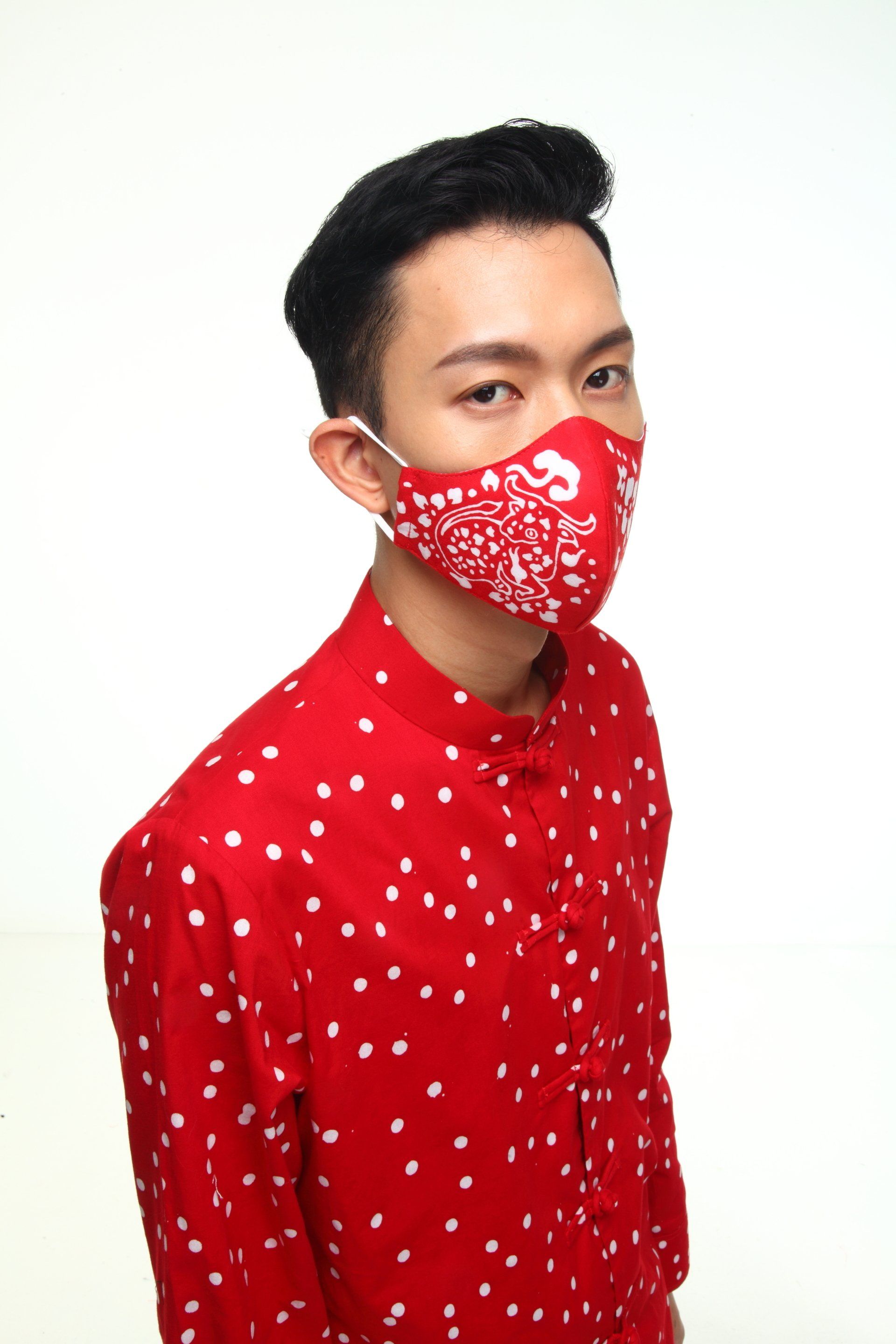 Person in red shirt and mask with white polka dots, looking at the camera. White backdrop.
