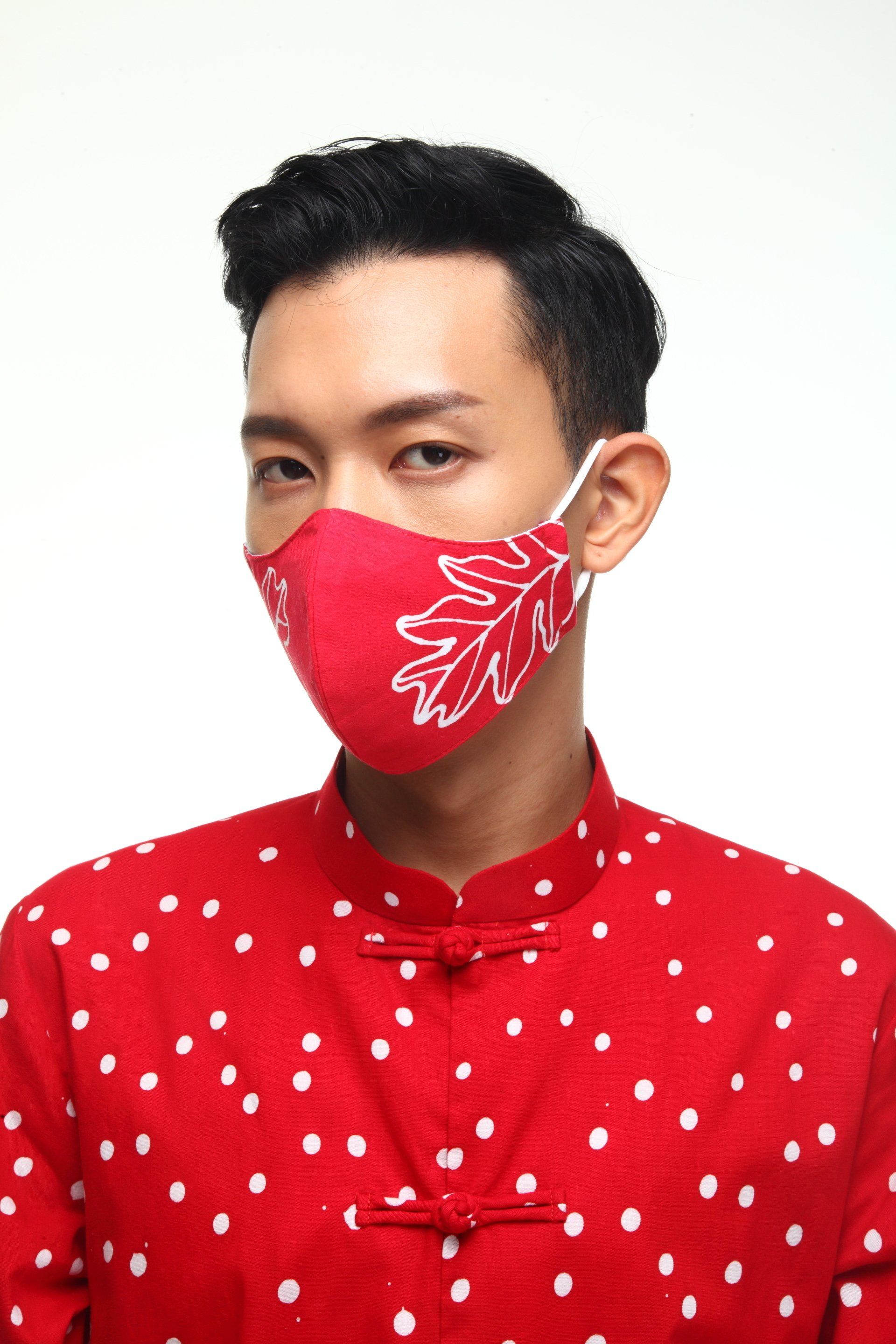 Man wearing a red face mask with white leaf design and red shirt with white polka dots.