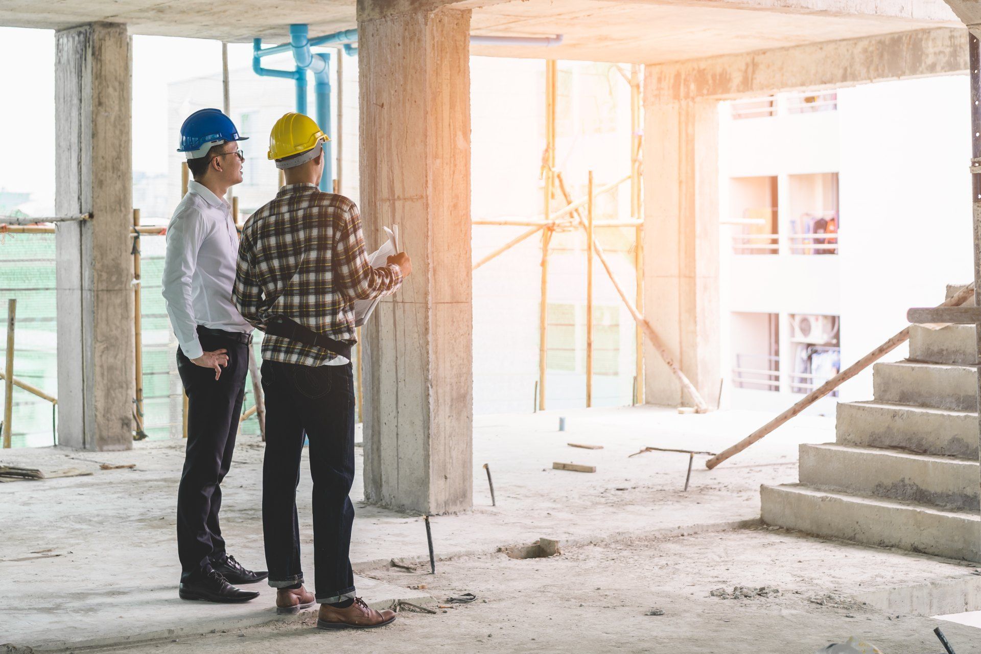 Two construction workers are standing in a building under construction.
