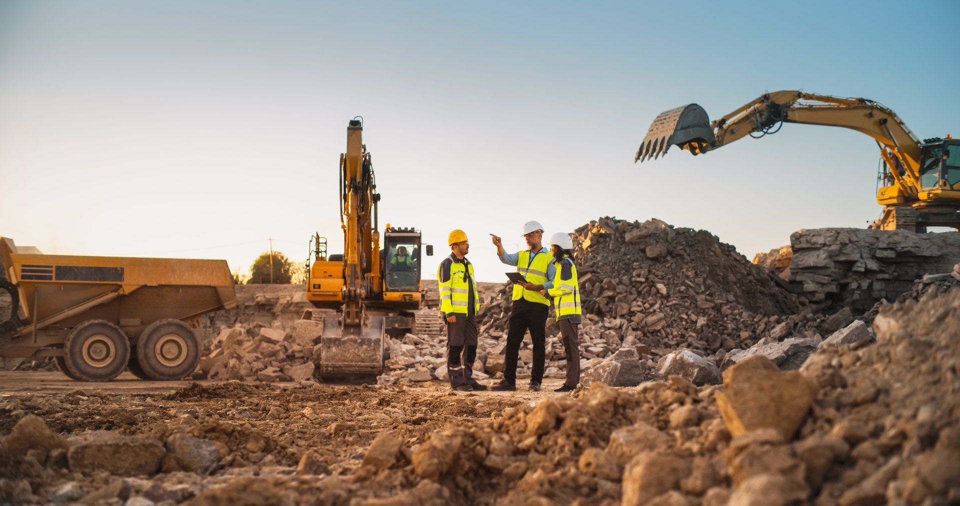 A group of construction workers are standing in front of an excavator at a construction site.