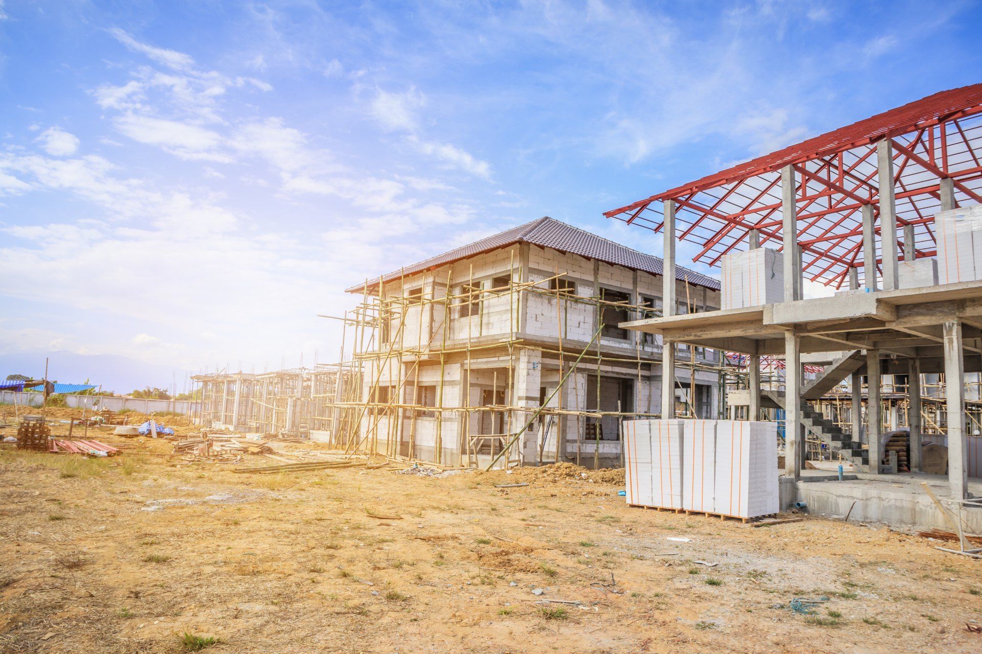 A group of houses are being built on a dirt field.