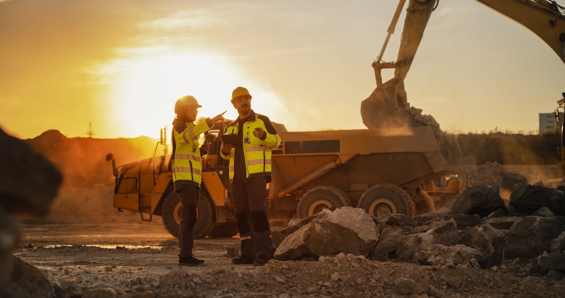 Two construction workers are standing in front of a bulldozer at a construction site.